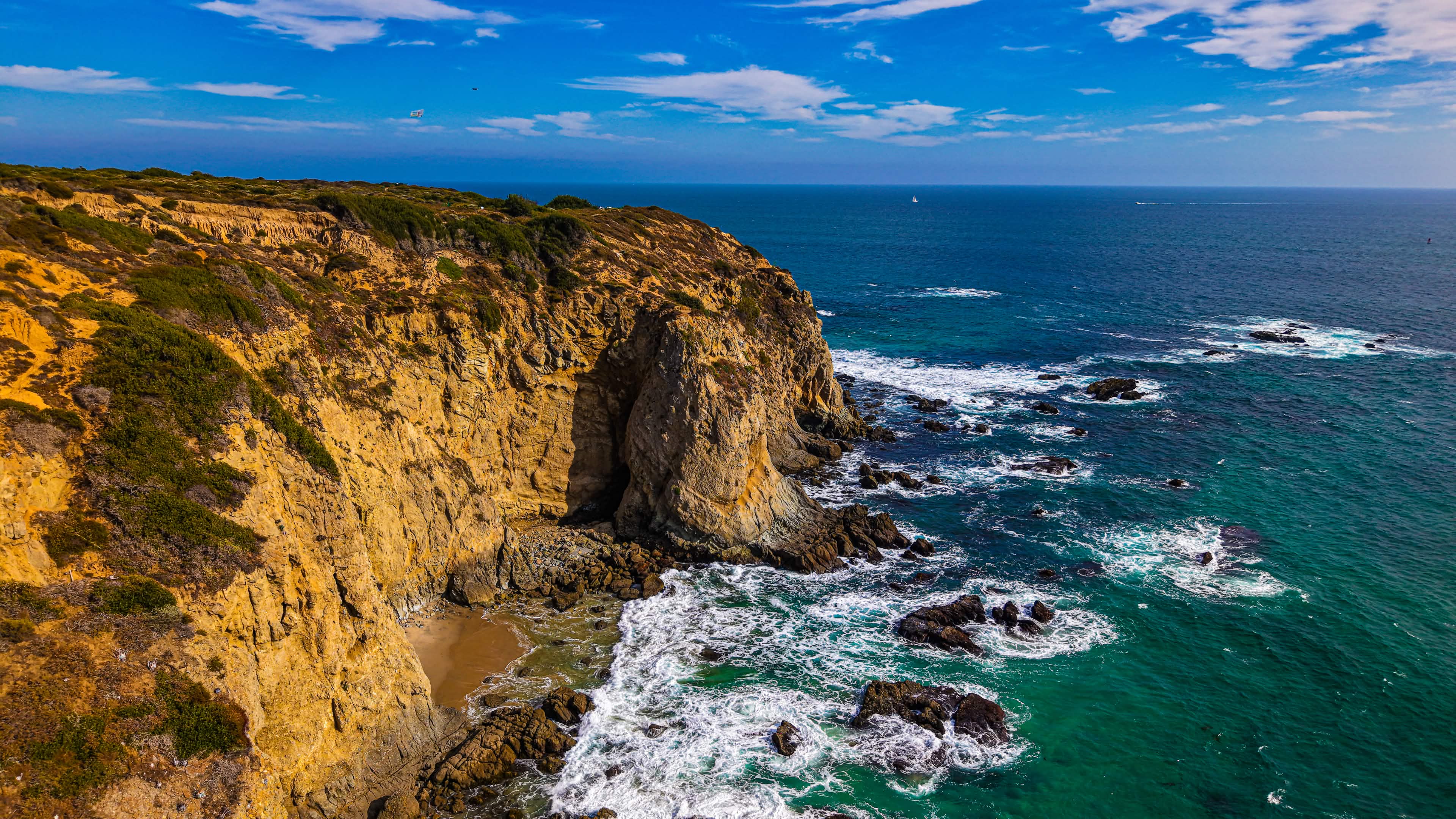 Aerial drone photograph of a rugged coastline — golden cliffs meeting turquoise ocean, shot on a DJI Air 3S