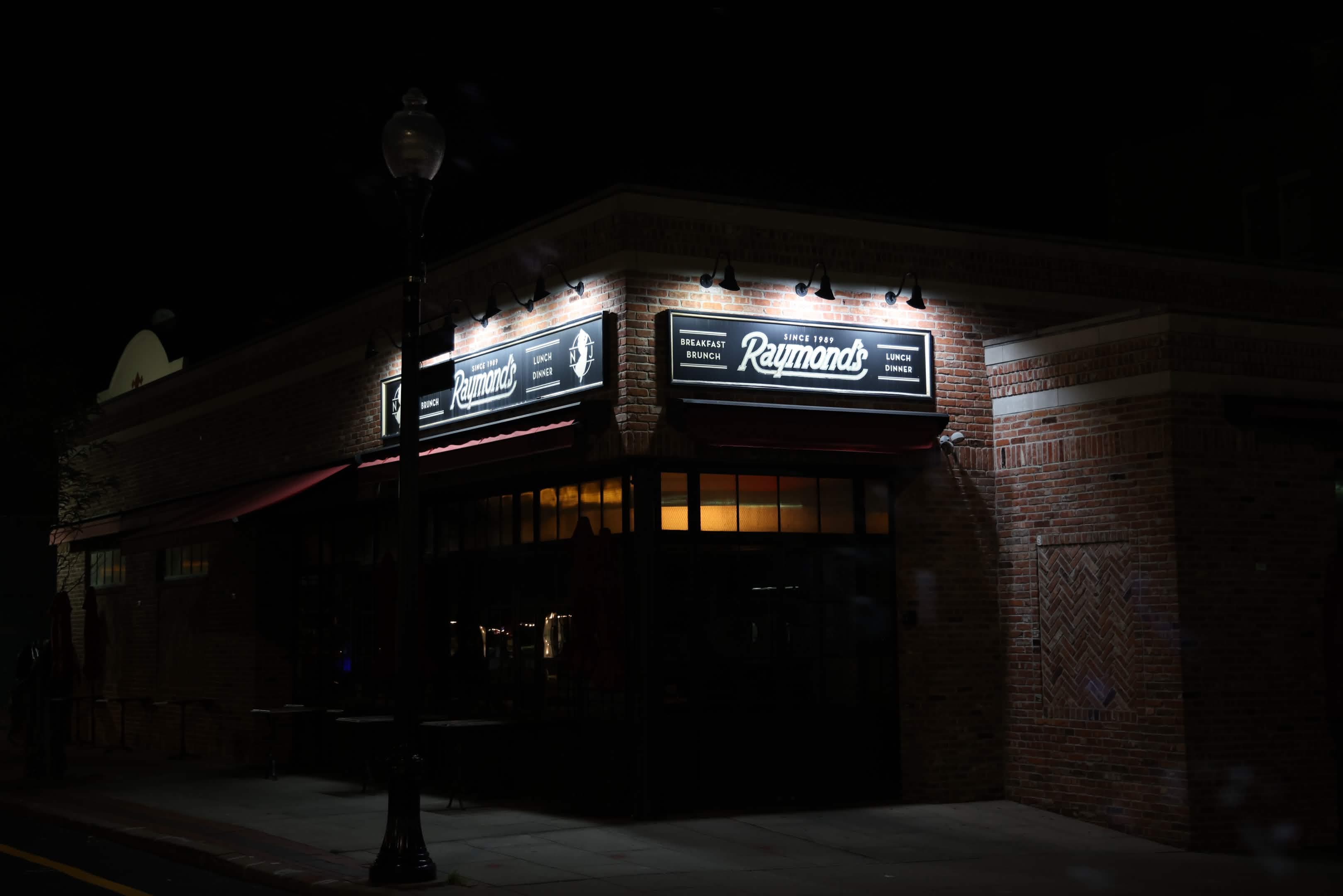 Night exterior of Raymond's restaurant in New Jersey — illuminated brick storefront and signage